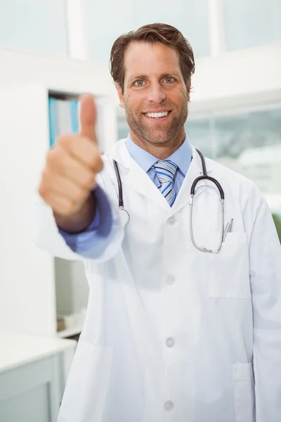 Sorridente medico maschio gesticolando pollici in alto a studio medico — Foto Stock