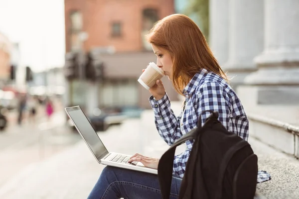 Kvinna dricker kaffe och använder bärbar dator utanför — Stockfoto