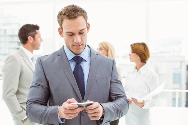 Businessman text messaging with colleagues in meeting behind — Stock Photo, Image