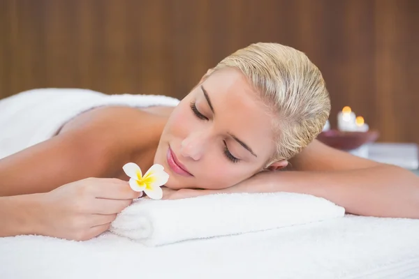 Mulher segurando flor na mesa de massagem — Fotografia de Stock