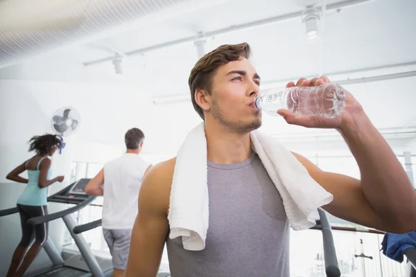 Fit man drinking water beside treadmills — Stock Photo, Image