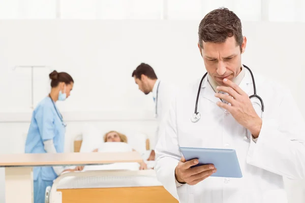 Doctor using digital tablet with colleagues and patient behind — Stock Photo, Image