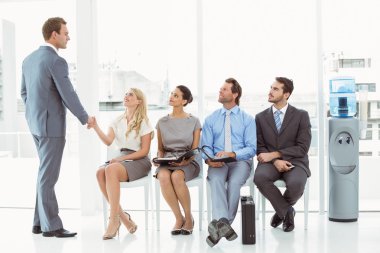 Businessman shaking hands with man besides people waiting for interview clipart