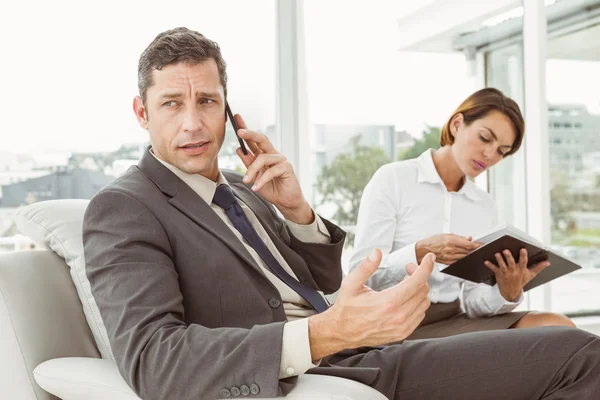 Businessman on call while secretary looks at diary — Stock Photo, Image
