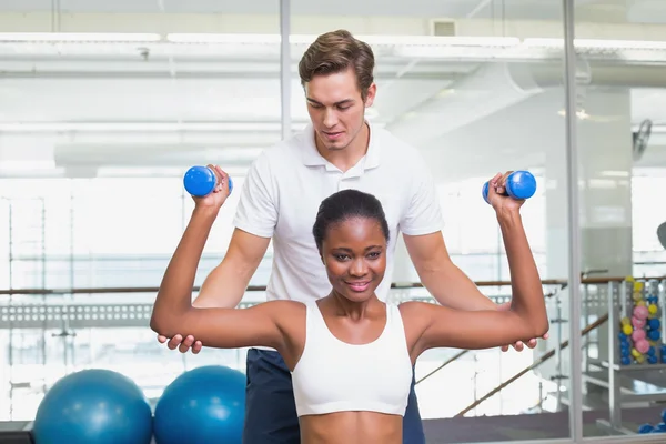 Personal trainer helping client lift dumbbells on exercise ball — Stock Photo, Image