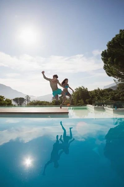 Alegre jovem casal pulando na piscina — Fotografia de Stock