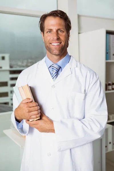 Médico varón sonriente sosteniendo libros en consultorio médico —  Fotos de Stock