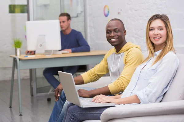 Casual colleagues using laptop on couch in office — Stock Photo, Image