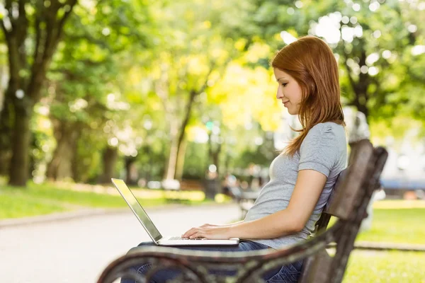 Happy girl sitting on bench using laptop — Stock Photo, Image