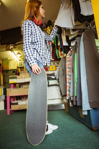 Girl looking at clothes while holding her skateboard — Stock Photo, Image