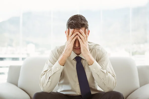 Hombre de negocios preocupado con la cabeza en las manos sentado en el sofá — Foto de Stock