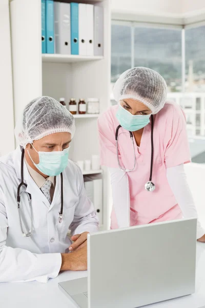 Doctors wearing surgical masks while using laptop at medical office — Stock Photo, Image