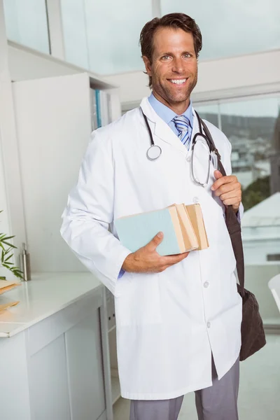 Médico varón sonriente sosteniendo libros en consultorio médico —  Fotos de Stock