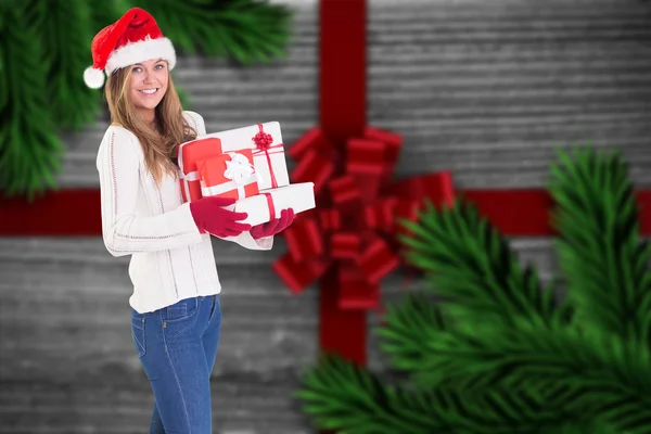 Zusammengesetztes Bild einer festlichen Blondine, die einen Haufen Geschenke in der Hand hält — Stockfoto