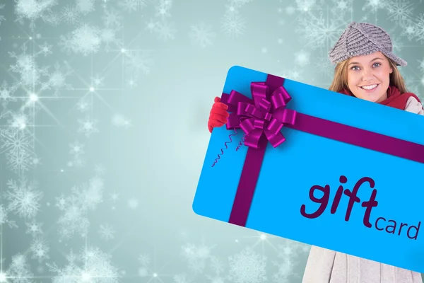 Imagen compuesta de la rubia feliz en ropa de invierno mostrando tarjeta — Foto de Stock