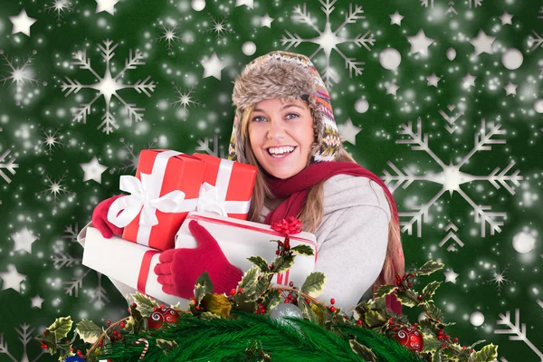 Composite image of happy blonde in winter clothes holding gifts — Stock Photo, Image