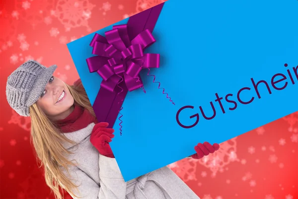 Composite image of happy blonde in winter clothes showing card — Stock Photo, Image