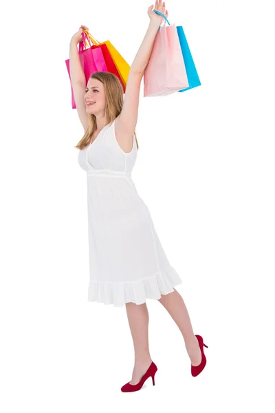 Excited blonde holding up shopping bags in white dress — Stock Photo, Image