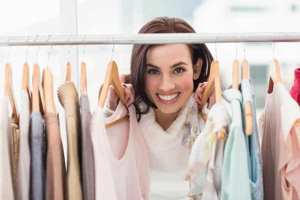 Beleza morena sorrindo para a câmera por trilhos de roupas — Fotografia de Stock