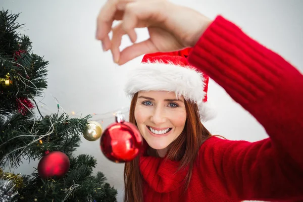 Festive redhead hanging bauble on tree — Stock Photo, Image