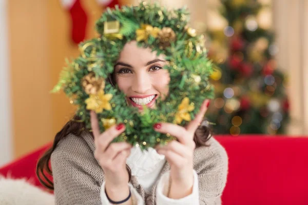 Brunette on the couch showing wreath at christmas — Stock Photo, Image