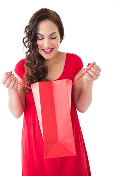 Elegante morena en vestido rojo apertura bolsa de regalo —  Fotos de Stock