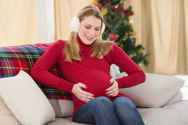 Schöne schwangere Frau hält ihren Bauch auf der Couch sitzend — Stockfoto