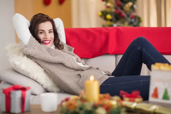 Улыбающаяся брюнетка отдыхает на диване на Рождество — стоковое фото