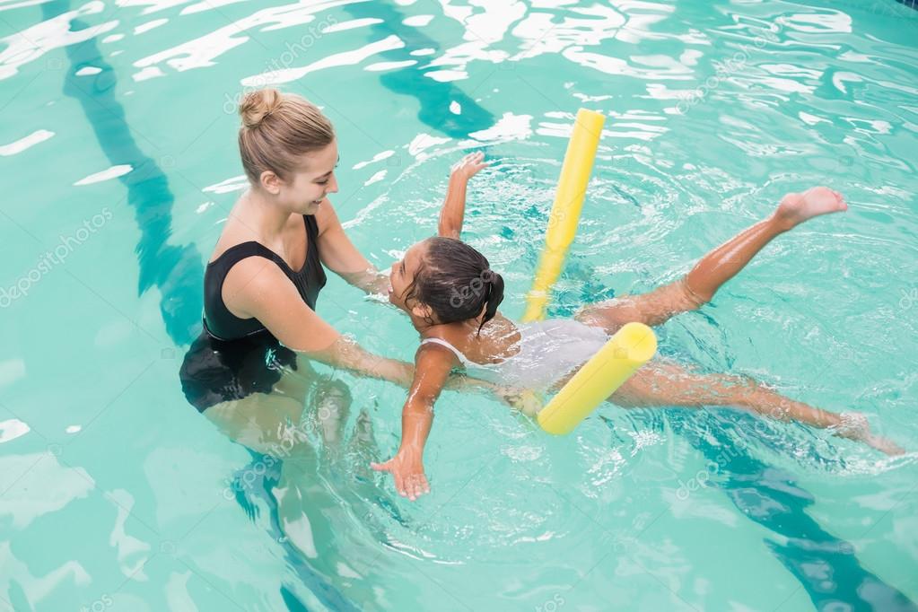 Cute little girl learning to swim with coach Stock Photo by