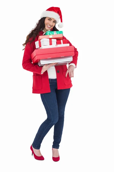 Morena festiva en sombrero de santa y abrigo rojo sosteniendo montón de regalos — Foto de Stock