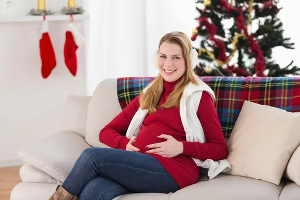 Beautiful pregnant woman holding her belly sitting on couch — Stock Photo, Image