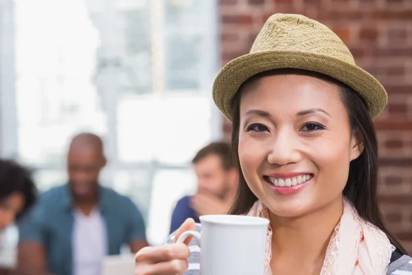 Vrouw met koffie beker met collega's achter in office — Stockfoto