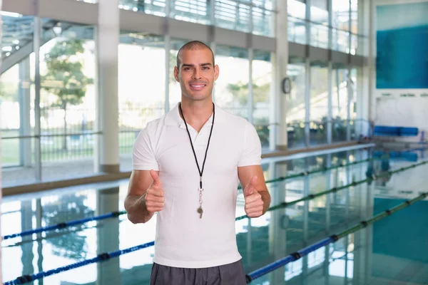 Swimming coach gesturing thumbs up by pool at leisure center — Stock Photo, Image