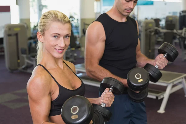 Pareja haciendo ejercicio con pesas en el gimnasio — Foto de Stock