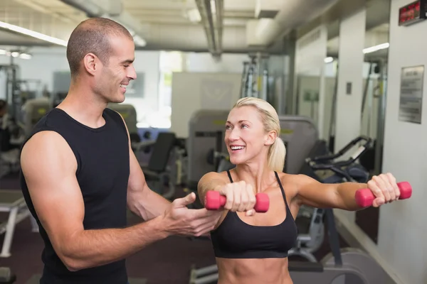 Entrenador masculino ayudando a mujer con mancuerna en el gimnasio — Foto de Stock