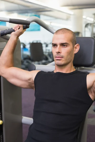 Sérieux jeune homme travaillant sur un appareil de fitness à la salle de gym — Photo