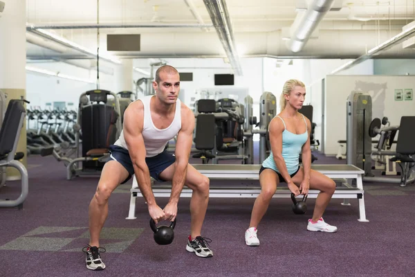 Fit couple lifting kettle bells in gym — Stock Photo, Image