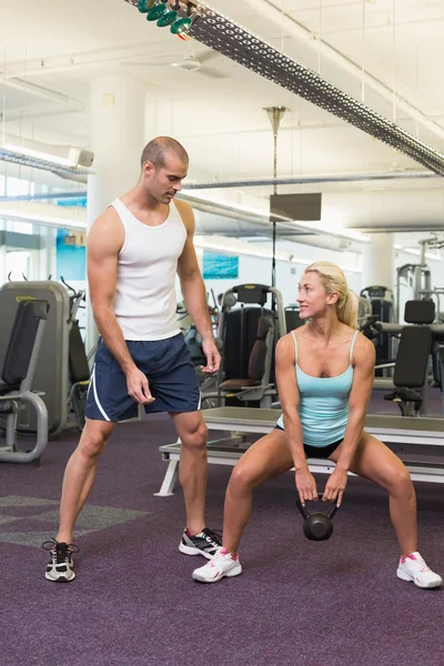 Trainer assisting woman with kettle bell in gym — Stock Photo, Image