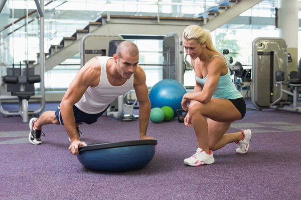 Female trainer assisting man with push ups at gym — Stock Photo, Image