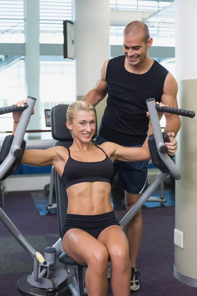 Treinador assistindo mulher na máquina de fitness no ginásio — Fotografia de Stock