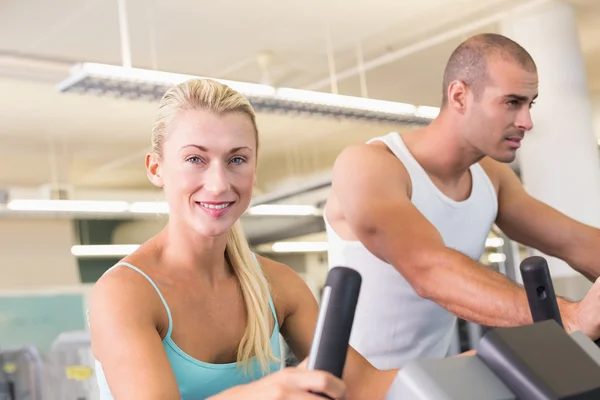 Ajuste pareja joven que trabaja en bicicletas estáticas en el gimnasio —  Fotos de Stock