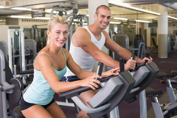 Ajuste pareja joven que trabaja en bicicletas estáticas en el gimnasio —  Fotos de Stock