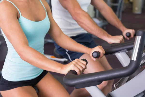 Mid section of couple working on exercise bikes at gym — Stock Photo, Image