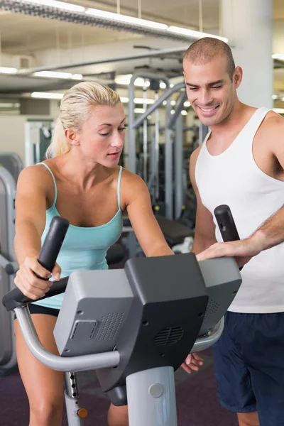 Trainer assisting woman with exercise bike at gym — Stock Photo, Image
