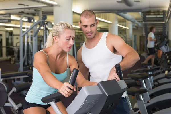 Entrenador ayudando a la mujer con bicicleta estática en el gimnasio —  Fotos de Stock