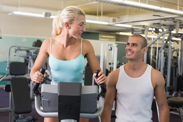 Entraîneur masculin aidant femme avec vélo d'exercice à la salle de gym — Photo