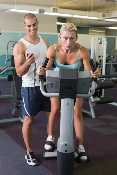 Trainer timing his client on exercise bike at gym — Stock Photo, Image