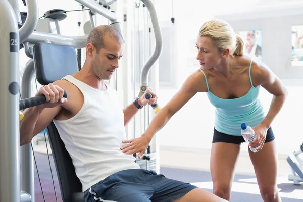 Entrenador que ayuda al hombre en la máquina de fitness en el gimnasio —  Fotos de Stock