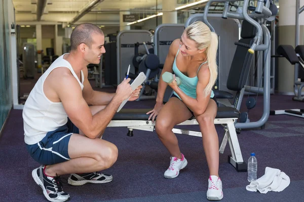 Entrenador masculino ayudando a mujer con mancuerna en el gimnasio —  Fotos de Stock