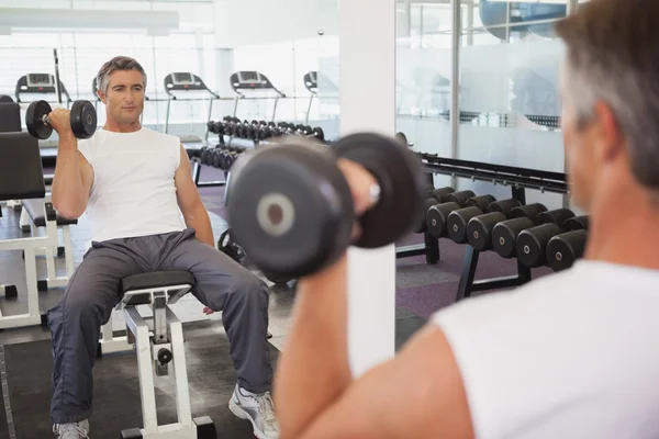 Hombre en forma levantando pesas sentado en el banco — Foto de Stock